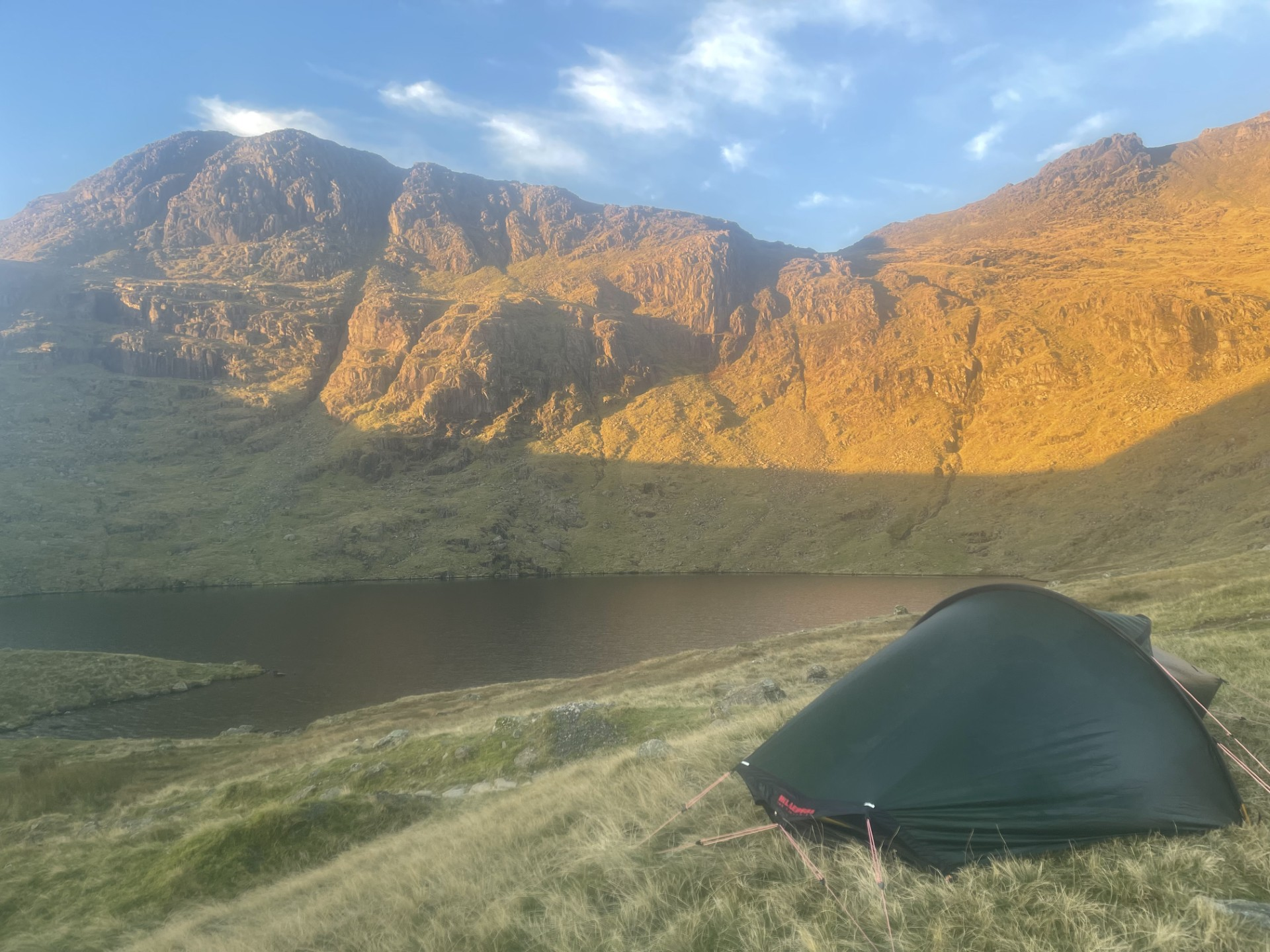 A wild camping tent beside a mountain lake in evening light